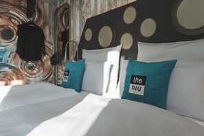 Una cama bien tendida con sábanas blancas y almohadas color turquesa, un cabecero de madera con diseños circulares, y una pared con un motivo abstracto ondulado.