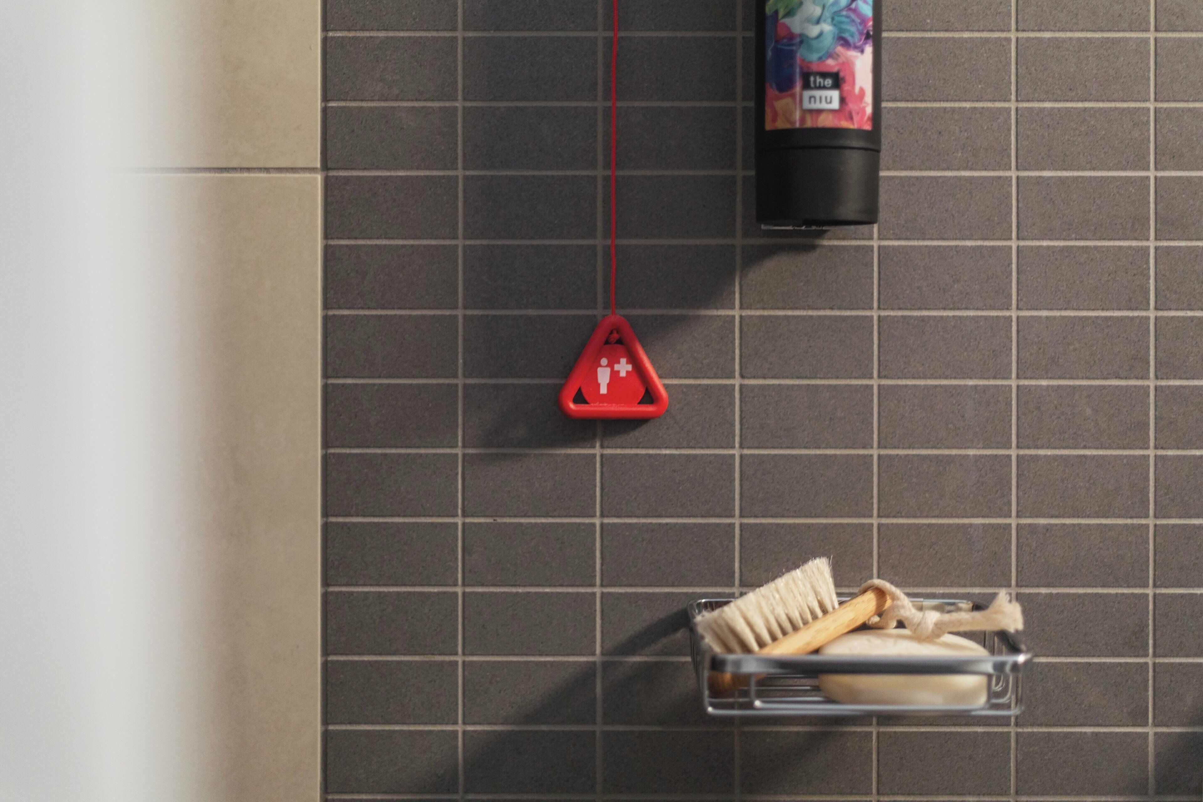 A bathroom with a tiled wall, a red safety sign, and a metal rack holding a toothbrush and a hairbrush.