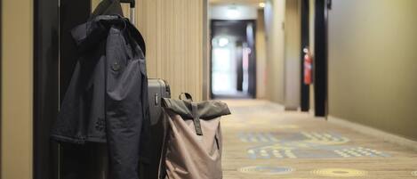 A hotel hallway with a luggage cart and a backpack near the wall.