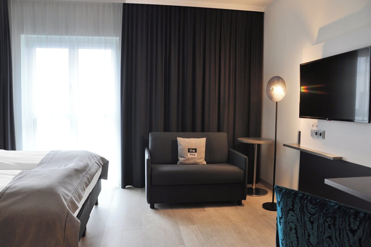 Una habitación de hotel moderna con cama, sofá, televisión y una pequeña mesa.