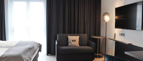 A modern hotel room with a bed, a sofa, a TV, and a small table.