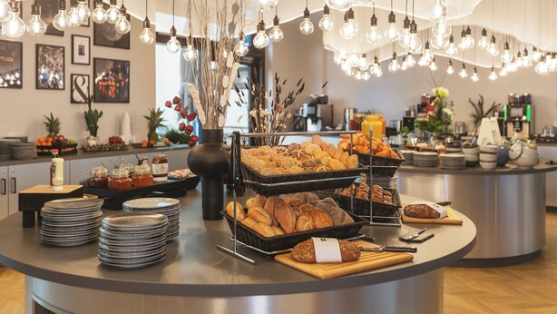 Zona de buffet con diferentes alimentos, platos y lámparas colgantes.
