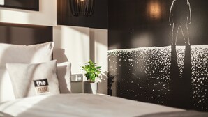 Un dormitorio moderno con una cama, almohadas, una mesita de noche con una planta y un cuadro de pared con una silueta.