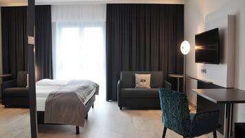 Habitació d'hotel moderna amb llit, sofà, escriptori i televisió.