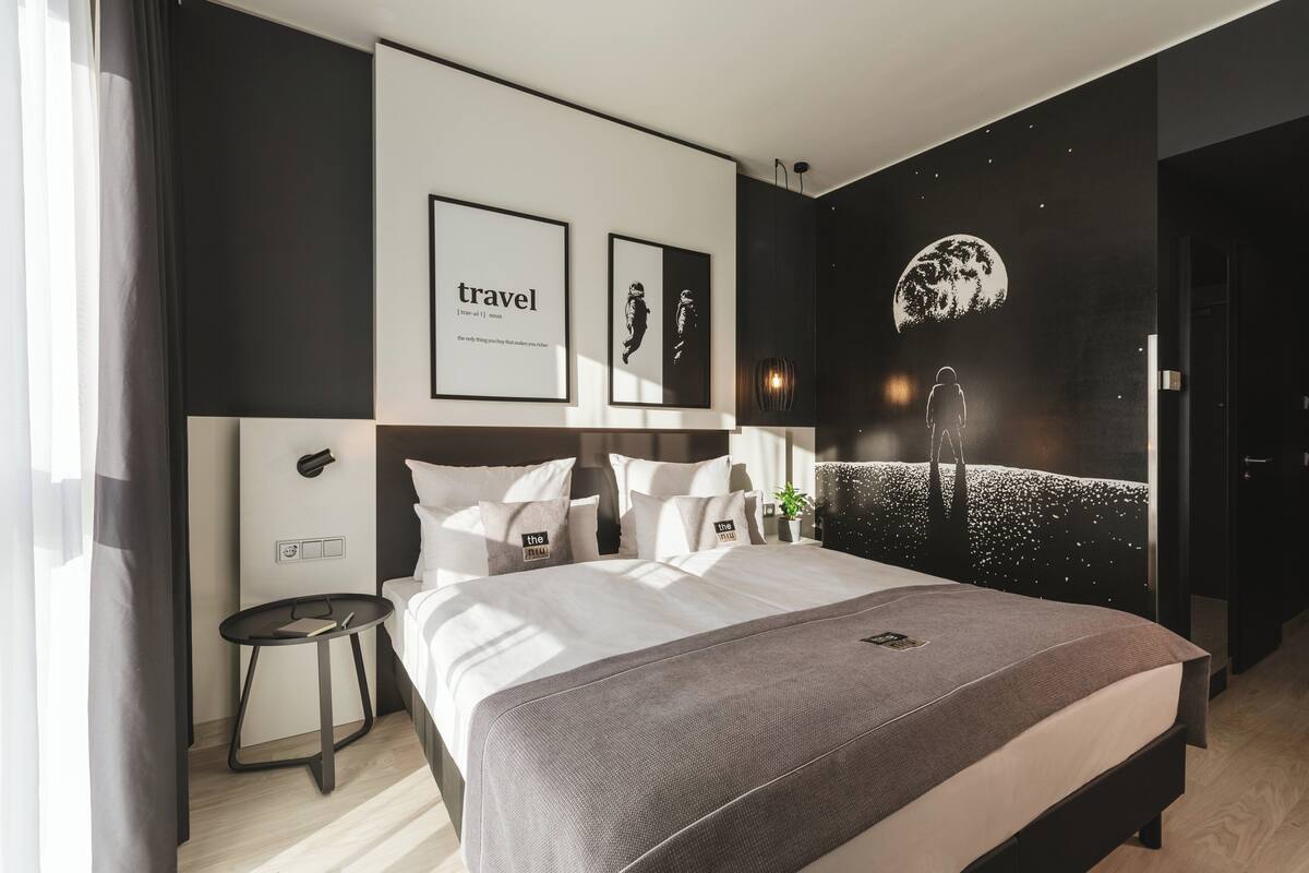 A modern hotel room with a large bed, a small side table, and a wall with framed artwork and a mural.