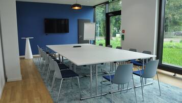 A conference room with a long table, chairs, a whiteboard, and a TV on the wall.