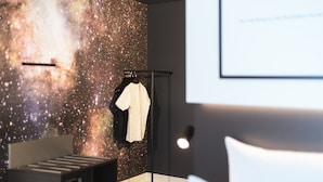 Habitación de hotel moderna con una pared temática de galaxia, un mueble de entretenimiento negro y una cama blanca.