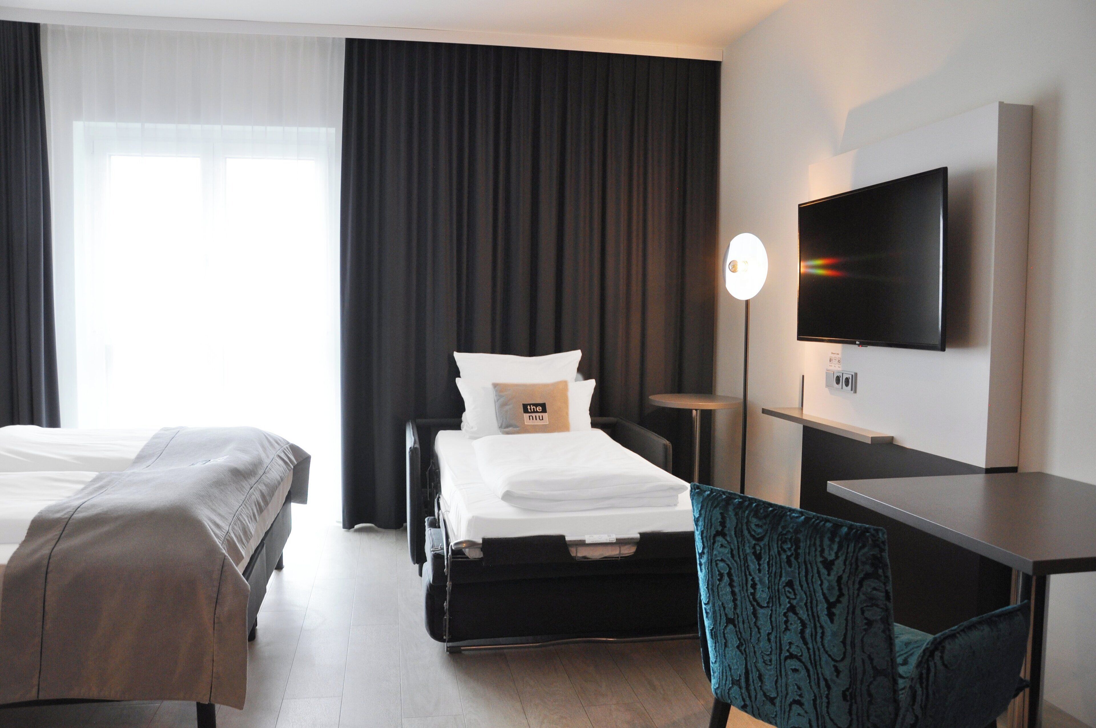 Quarto de hotel com duas camas, uma escrivaninha, uma televisão e um abajur.