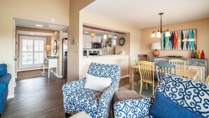 Amplia sala de estar con sofás estampados, una zona de comedor con mesa y sillas de madera, y una cocina al fondo.