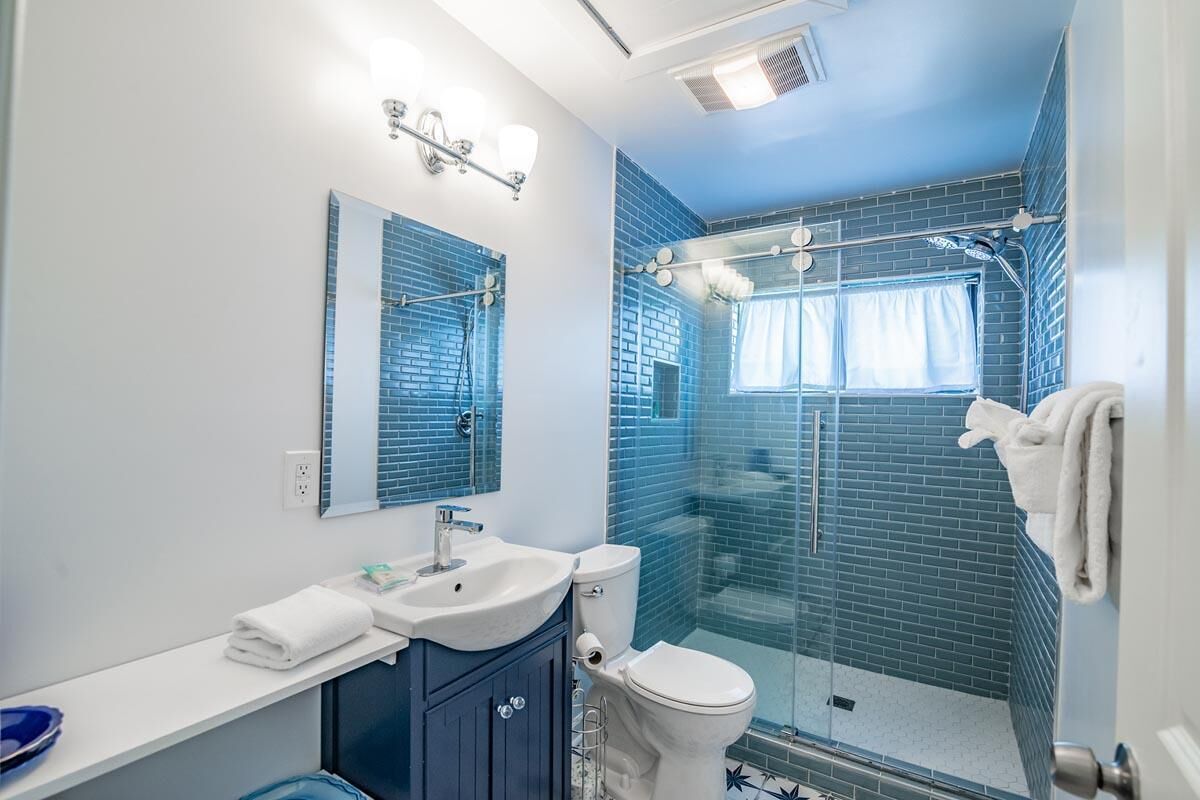 A bathroom with a sink, mirror, and toilet. There is a glass shower enclosure with a window.