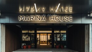 The exterior of Marina House with a modern design, featuring a prominent illuminated sign and a welcoming entrance with steps and potted plants. - Marina House MUAYTHAI Ta-iad Phuket (Chalong)