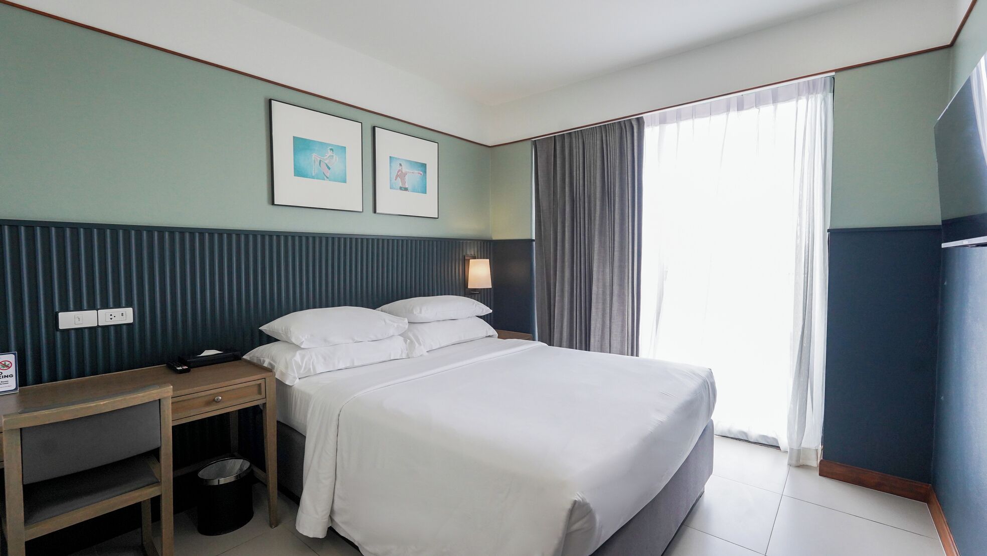 A hotel room with a bed, bedside table, lamp, and two framed pictures on the wall.