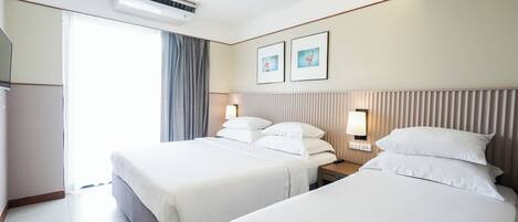 A hotel room with two beds, a large window, an air conditioning unit, and two framed pictures on the wall.