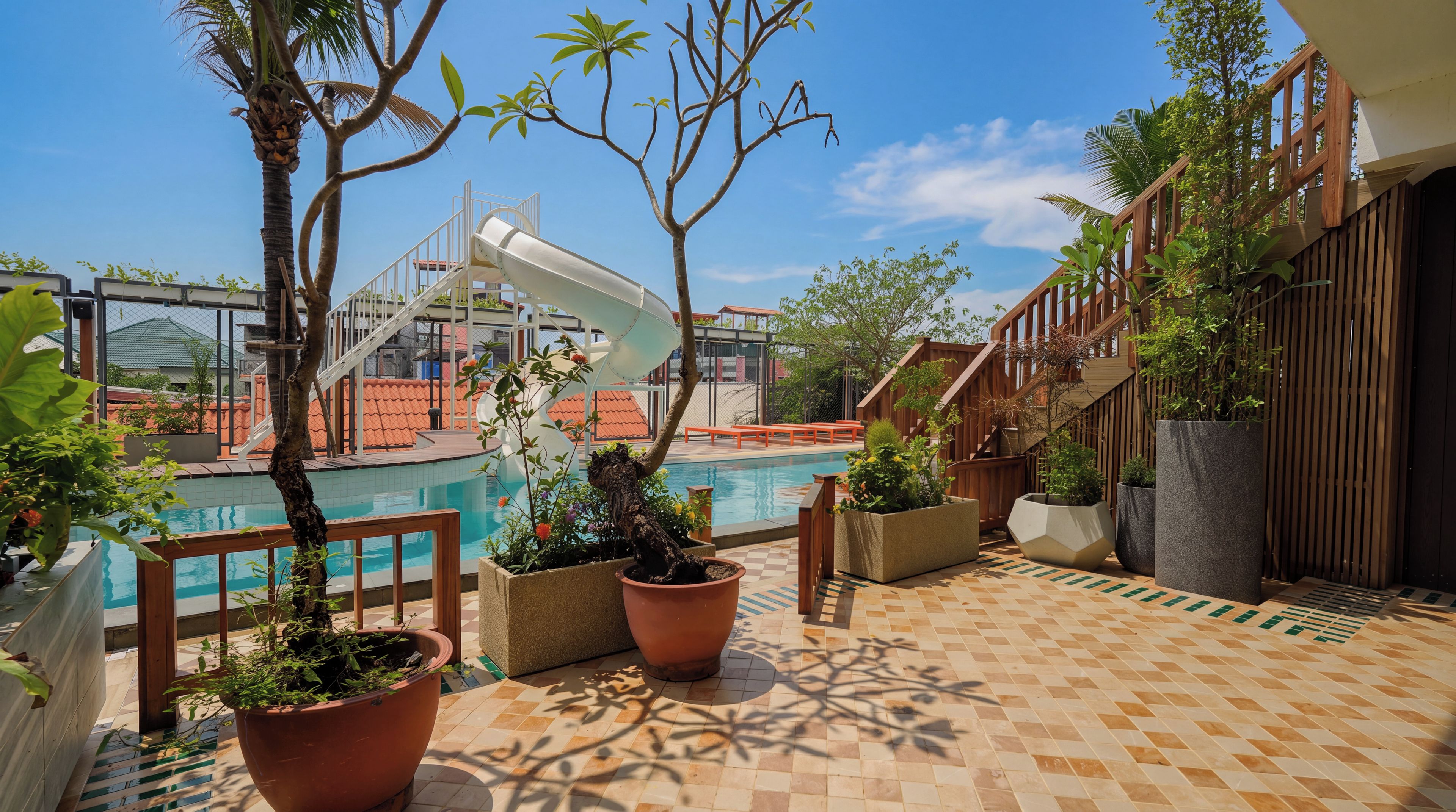 A pool area with a slide, potted plants, and a wooden deck.