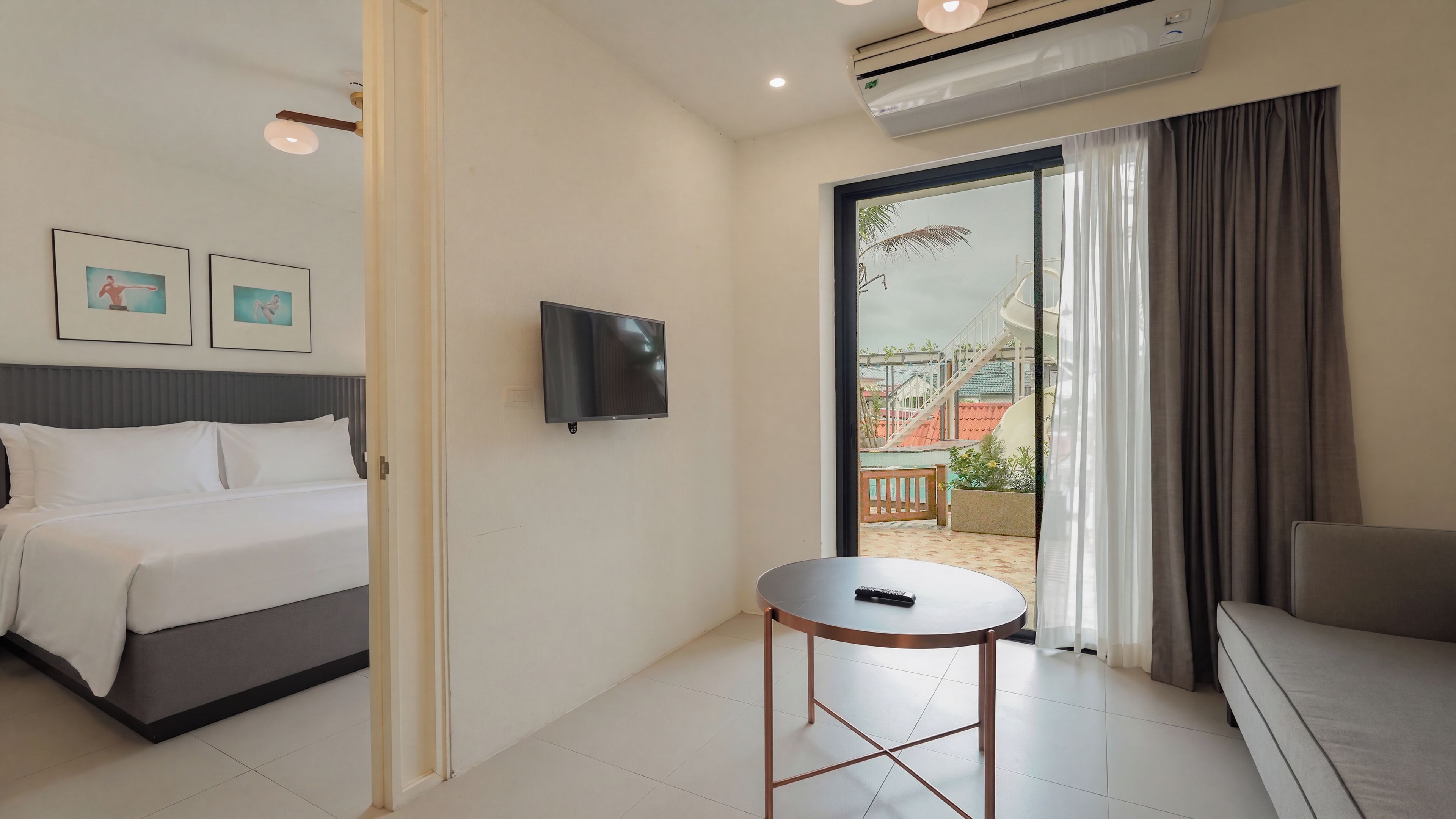 A hotel room with a bed, a TV, a small table, and a view of the outside.