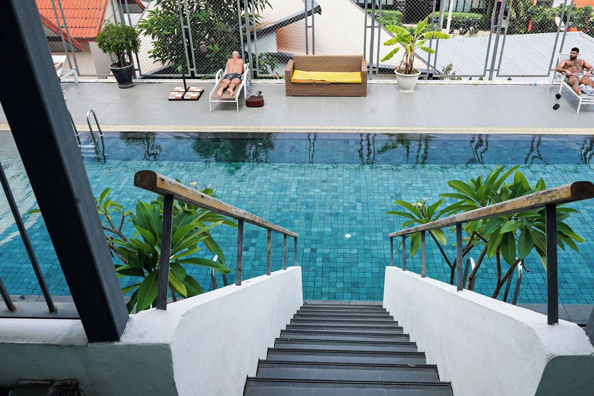 A pool area with a staircase leading down to the water, lounge chairs, and potted plants.