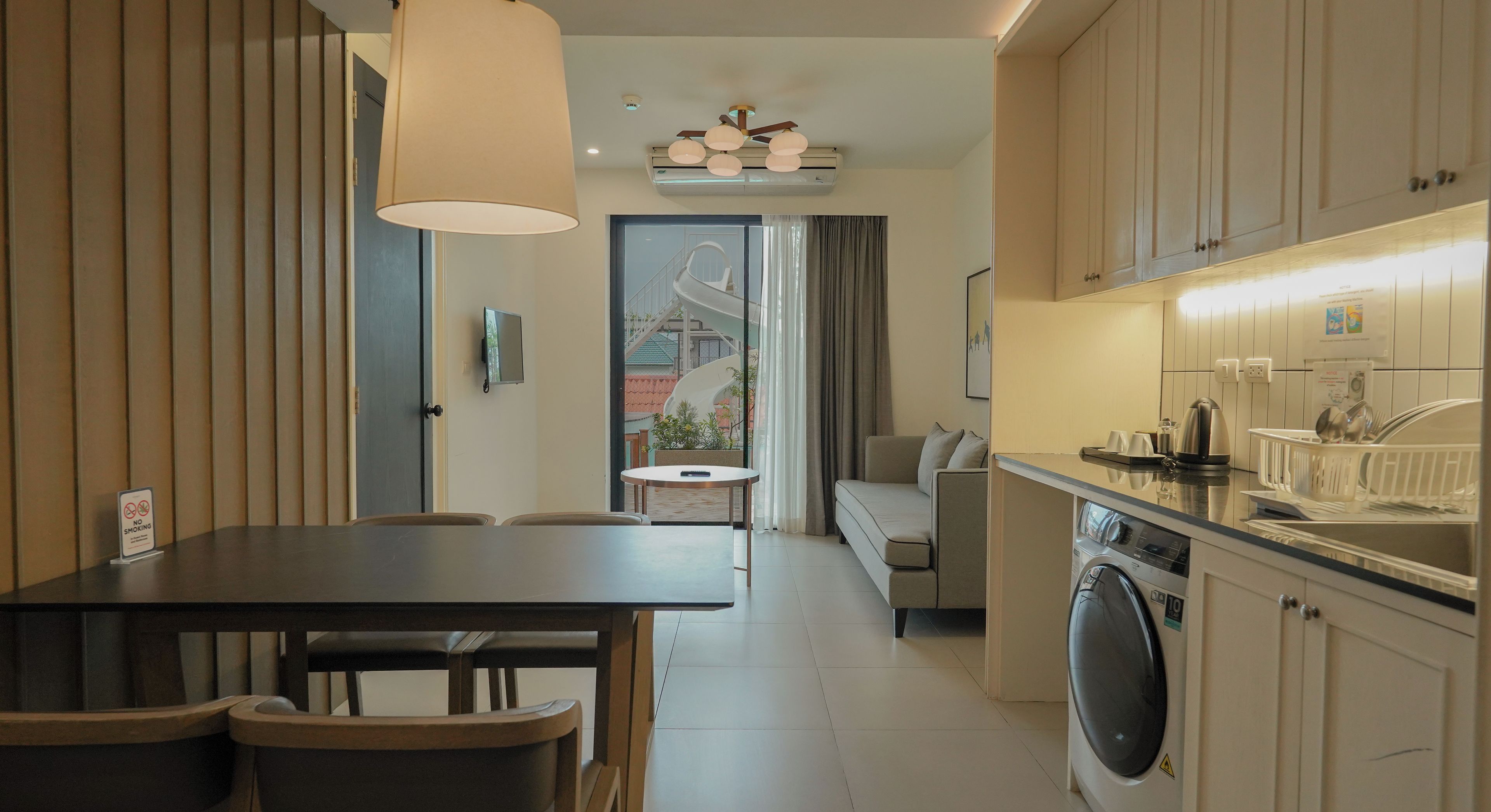 A modern kitchen with a washing machine, dining area with chairs, and a view of a building outside.