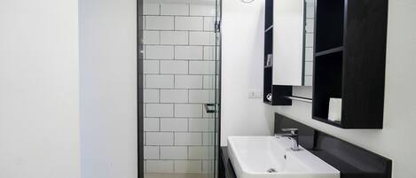 A modern bathroom with a white sink, black countertop, and a glass shower enclosure.