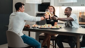 A modern kitchen with white cabinets, a dark countertop, and a central island with a person toasting with a glass. - Marina House MUAYTHAI Ta-iad Phuket (Chalong)