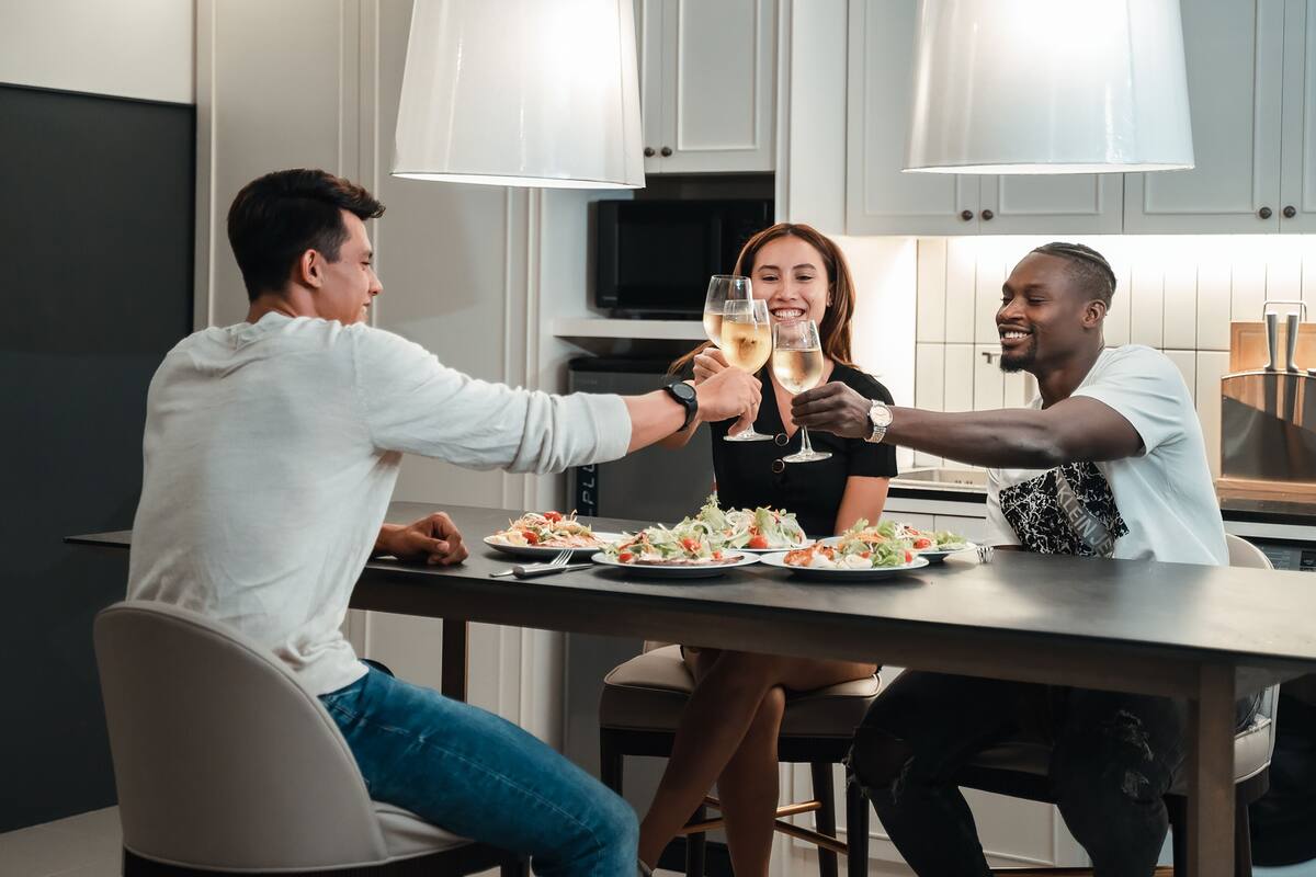 A modern kitchen with white cabinets, a dark countertop, and a central island with a person toasting with a glass.