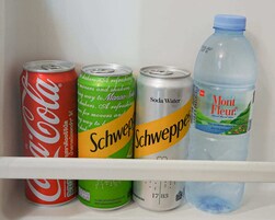 Una estantería con cuatro latas de bebida y una botella de agua.