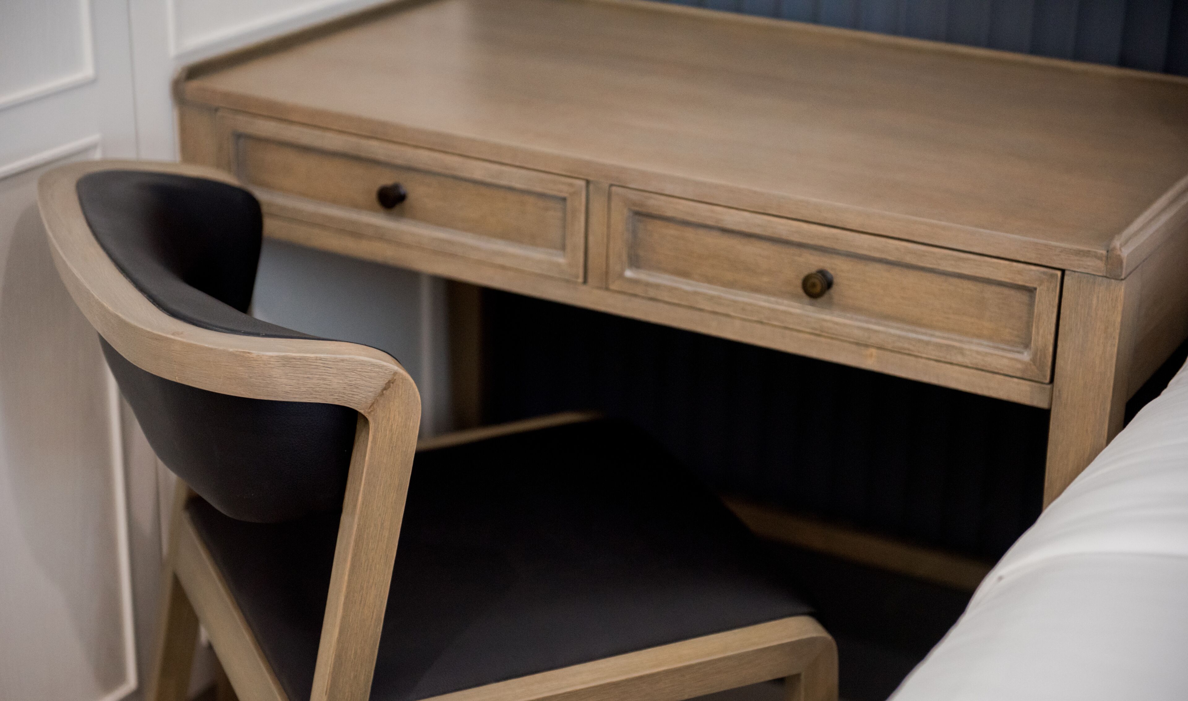 A wooden desk with two drawers and a black chair with a wooden frame.