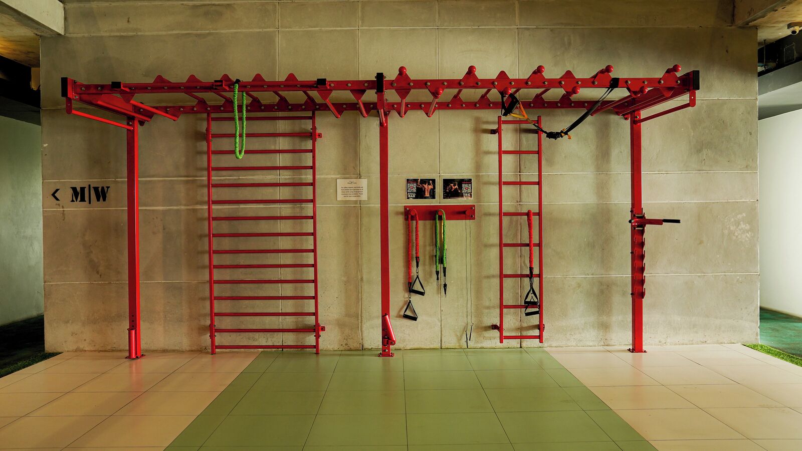 Un gimnasio con equipo de ejercicio rojo, incluyendo una barra de dominadas, una escalera y bandas de resistencia.