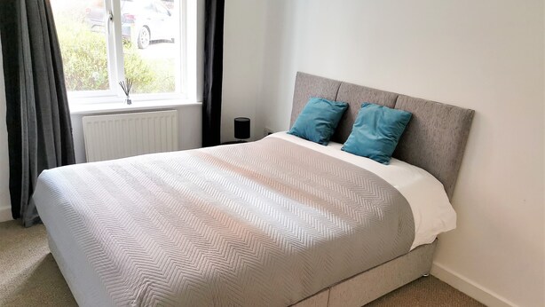 Un lit bien fait, avec une couvre-lit à motifs, deux oreillers et une table de chevet surmontée d’une lampe.