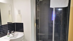 Une salle de bain avec un lavabo blanc, un miroir et une douche séparée par des parois en verre, le tout agrémenté de carreaux noirs.