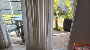 Une pièce avec un sol carrelé, une table avec des magazines et une vue sur l’extérieur par une fenêtre ornée de rideaux.