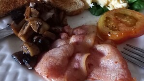 Une assiette avec des toasts, des œufs brouillés, des champignons, du bacon et une tranche de tomate.