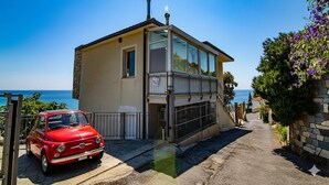 A two-story house with a balcony, a red car parked in front, and a view of the sea. - Casa Baia Blu (San Lorenzo al Mare)