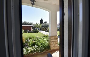 A view through a doorway to a garden with a pathway, a brick wall, and a building in the background.