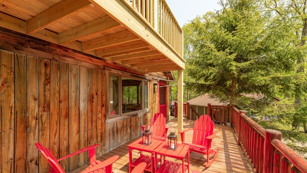Eine Holzterrasse mit roten Stühlen und Tischen, mit Blick auf eine bewaldete Gegend.