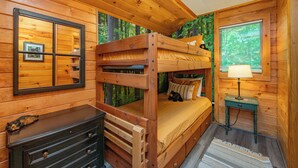 Ein Schlafzimmer einer Holzhütte mit einem Etagenbett, einem Schminktisch, einem Spiegel und einem Fenster mit Jalousien.