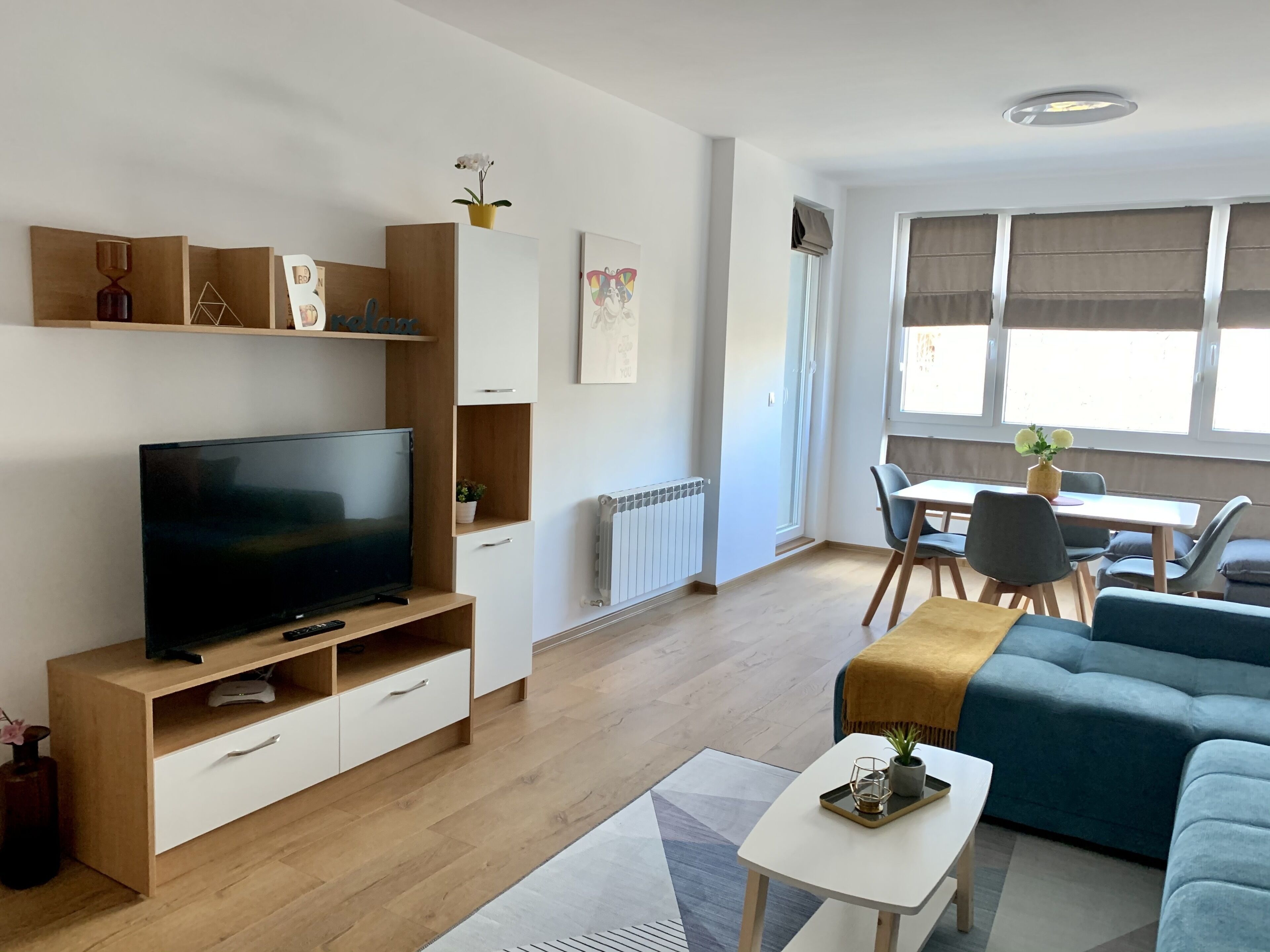 A modern living room with a flat-screen TV, wooden furniture, a sofa, and a dining area with a table and chairs.