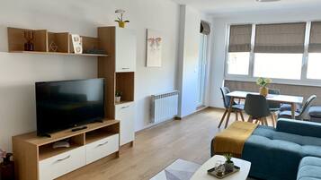 A modern living room with a flat-screen TV, wooden furniture, a sofa, and a dining area with a table and chairs.