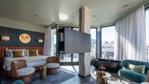 Una habitación de hotel moderna con una cama grande, una bañera y una zona de estar con sillones y un sofá.