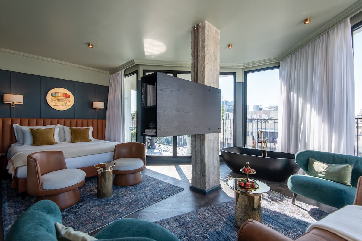 Una habitación de hotel moderna con una cama grande, una bañera y una zona de estar con sillones y un sofá.