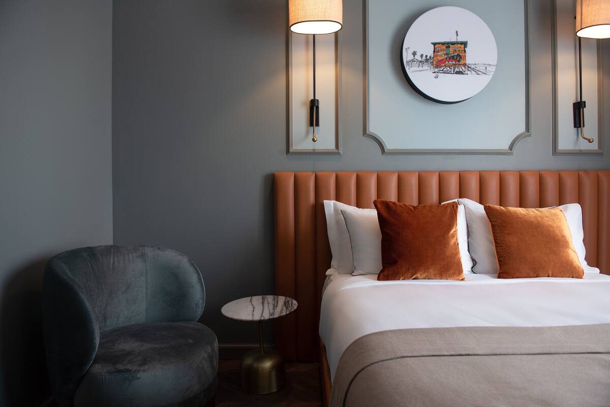 Habitación de hotel con cama, una silla, una mesita redonda y lámparas fijadas a la pared.