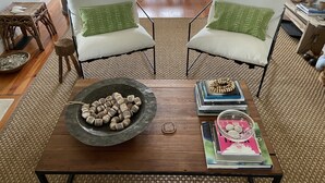 A living room with two white armchairs, a wooden coffee table with decorative items, and a woven rug. - Fun Beach House (Sullivans Island)