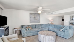 A living room with a sectional sofa, a round coffee table, a TV, and artwork on the wall.