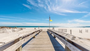 A wooden boardwalk leading to a beach with a flagpole and a flag.