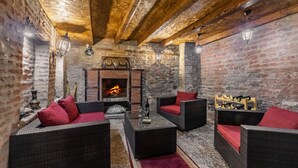 Une pièce chaleureuse, meublée de meubles en osier, agrémentée de coussins rouges, dotée d’une cheminée et de murs en pierre.