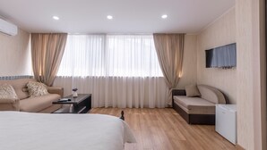 Une chambre d’hôtel moderne équipée d’un lit, d’un canapé, d’une petite table, d’une télévision et d’un mini-réfrigérateur.
