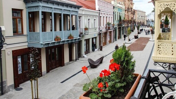Une rue bordée de bâtiments historiques, une place centrale et un petit jardin agrémenté de fleurs rouges.