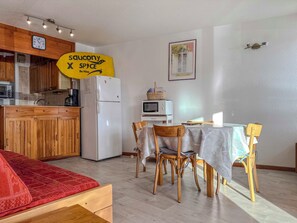 A compact kitchen with wooden cabinets, a white refrigerator, a microwave, and a dining area with a table and chairs.