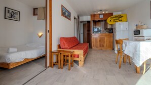 A compact room with a bed, a red sofa, a small wooden table, and a kitchenette area. - #AH3 | The Snow White ❄ (Huez)