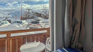 A view from a window with a wooden deck and a table, overlooking a snowy parking area with cars and a ski lift in the background. - #AH3 | The Snow White ❄ (Huez)