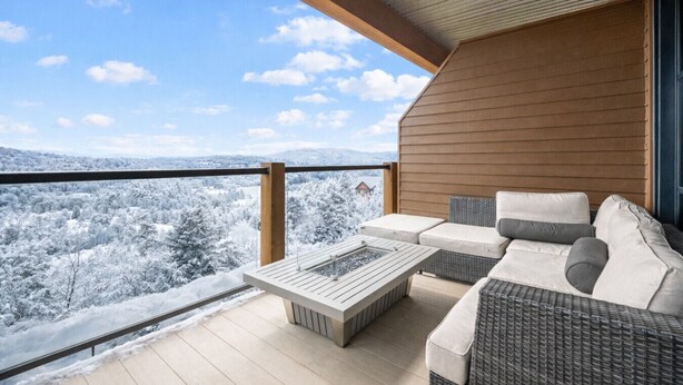 Un balcon donnant sur un paysage enneigé, un plafond en bois et un coin salon avec une table.